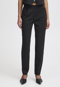 Black tailored trousers with flat front, smooth texture, slim fit, and ankle-length design, paired with pointed black heels.