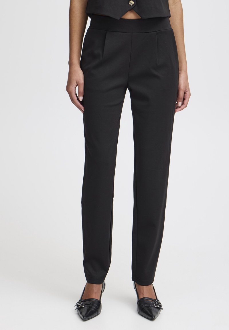 Black tailored trousers with flat front, smooth texture, slim fit, and ankle-length design, paired with pointed black heels.