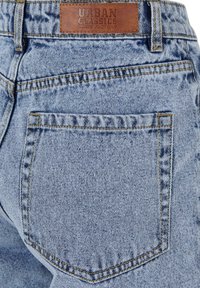 Light blue denim jeans back pocket with brown leather Urban Classic Denim Factory brand label above the waistband.