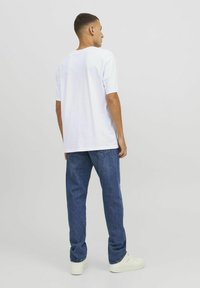 Witte t-shirt met korte mouwen en ronde hals, gecombineerd met blauwe denim jeans. Het model draagt witte sneakers. Effen stof, ontspannen pasvorm.