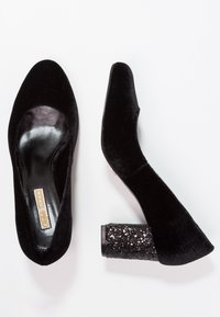 Chaussures à talons hauts en velours noir avec un bout arrondi, dotées d'un talon en bloc pailleté texturé et d'un intérieur lisse noir.
