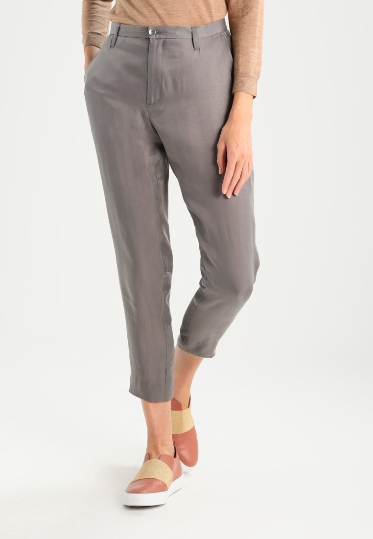 Light grey trousers with a smooth texture, featuring a button closure and cropped design. Paired with slip-on shoes in pink and gold accents.
