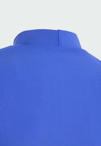 Modrá polo tričko s krátkým límečkem, hladkým povrchem a jednoduchým designem bez viditelných vzorů nebo kovových prvků.