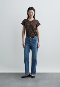 T-shirt de estampa de leopardo castanha com mangas curtas, combinada com jeans azul claro decorados com tachas decorativas. Sapatos baixos pretos completam o visual.