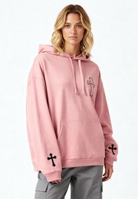 Felpa oversize rosa in cotone con tasca frontale. Presenta dei design neri a croce sulle maniche e un piccolo logo a croce sul petto.