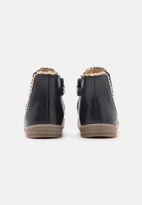 Námořnické kožené kotníkové boty s rýhovaným hnědým lemem, zipem a gumovými podrážkami s texturovaným vzorem na spodní straně.