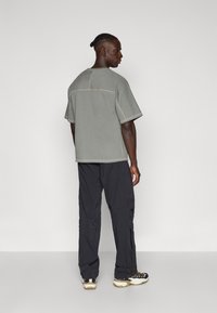 Harmaa lyhythihainen t-paita, jossa on kontrastiväriset saumat ja rento malli, yhdistettynä mustiin housuihin ja urheilukenkiin, joissa on vaaleanbeigejä korostuksia.