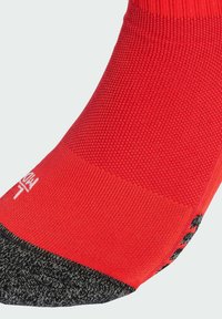 Calcetín rojo hecho de una tela texturizada, con la puntera y el talón negros. Tiene patrones tejidos y un logo blanco cerca del puño.