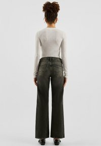 Schwarze Jeans mit weitem Bein, hoher Taille und fünf Taschen, kombiniert mit einem cremefarbenen Langarmshirt mit kleinen Verzierungen.