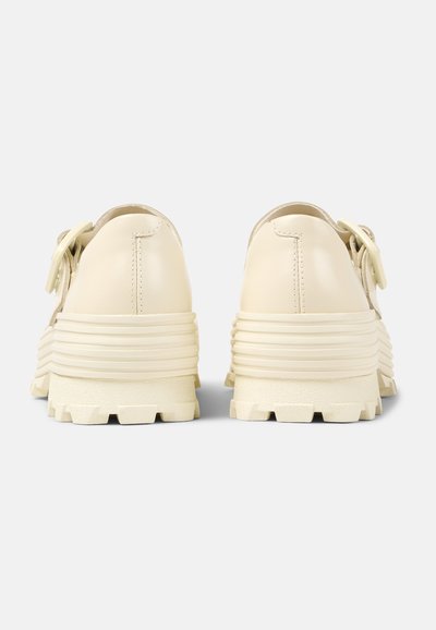 Cream-colored leather shoes with a ridged sole and thick platform. Feature a rounded toe and decorative hardware on the side.
