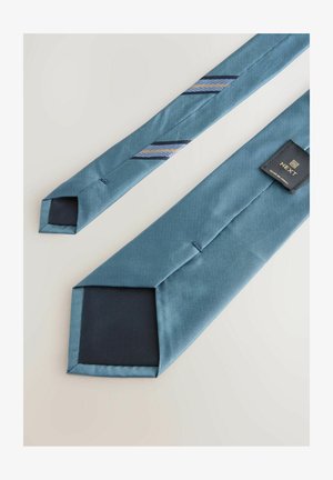 Eine blaue Krawatte mit strukturierter Oberfläche, die diagonale Streifen in Marineblau und Gold aufweist. Die Krawatte hat ein quadratisches Ende und ein angebrachtes Etikett.