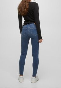 Blauwe denim skinny jeans met een middelhoge taille, voorzien van twee achterzakken en een gladde textuur. Compleet met witte sneakers.