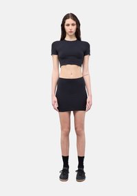 Maglietta nera corta abbinata a una mini gonna aderente nera. L'outfit presenta una texture di cotone liscia e una silhouette aderente. Sneakers nere completano il look.