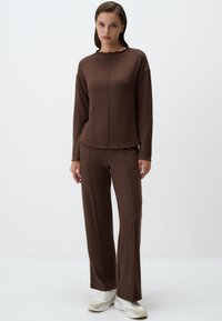 Completo in maglia marrone a due pezzi, composto da un top a maniche lunghe con scollo a ondine e pantaloni a gamba larga abbinati, entrambi con dettagli cuciti.