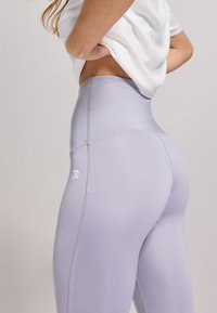 Hoge taille lavendelkleurige legging van rekbaar materiaal, met een strakke pasvorm, een gladde textuur en een klein wit logo aan de zijkant.