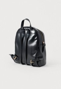 Mochila de cuero sintético negro con forma redondeada, dos asas superiores, cierre con cremallera, correas ajustables y detalles en metal dorado.