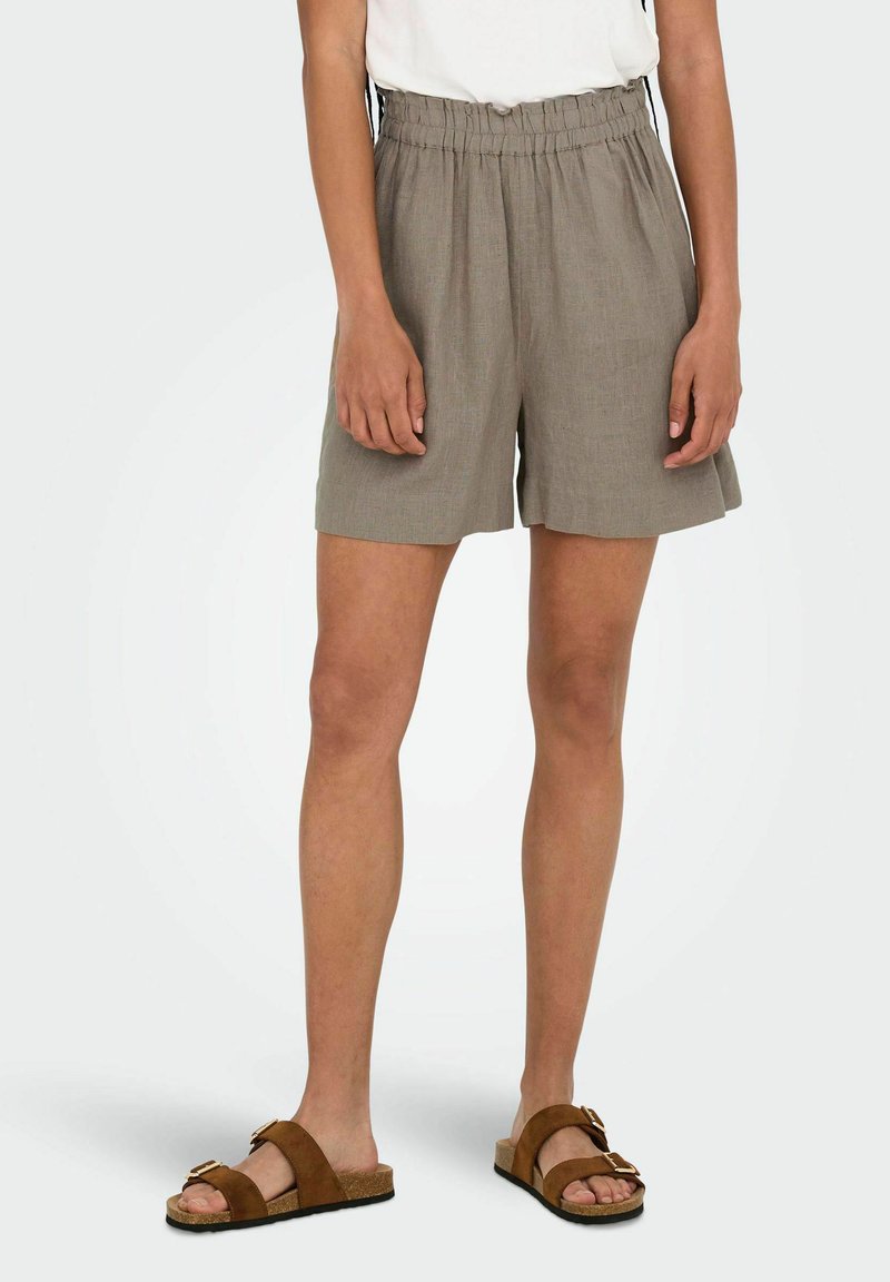 Pantaloni corti leggeri di colore khaki con vita elastica e tasche laterali. Indossati con sandali marroni con un dettaglio a fibbia.