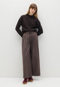 Suéter marrón oscuro con un cuello alto, combinado con pantalones de cuadros anchos en tonos marrón y crema. Zapatos burdeos con suelas beige completan el conjunto.