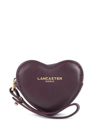 Porte-monnaie en cuir violet foncé en forme de cœur avec logo doré Lancaster Paris et bracelet pour poignet sur fond blanc.