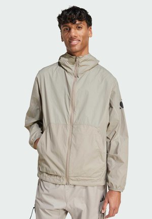 Letvægts beige jakke med lynlås, elastiske manchetter og hætte; har sidelommer og en sort logoaccent på ærmet.