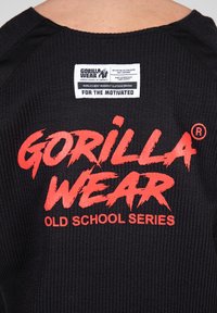 Zwarte sportshirt met geribbelde textuur. Heeft een groot rood 'GORILLA WEAR' logo en label met merkdetails.