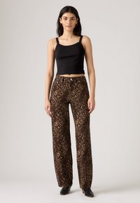 Črni prirezani top brez rokavov v kombinaciji z rjavimi širokimi hlačami z leopardjim potiskom. Hlače imajo teksturo, ki spominja na mehko tkanino, in kovinske gumbe.