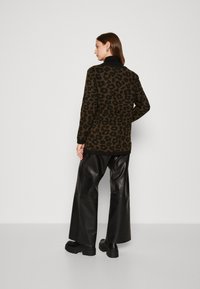 Een luipaardprint trui in donkerbruin en zwart, van gebreid materiaal, met lange mouwen en een relaxed fit, gecombineerd met wijde zwarte leren broeken en stevige laarzen.