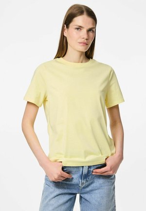 Gul bomulds T-shirt med rund hals og korte ærmer, iført med højtaljede lyseblå jeans. Blødt tekstur, enkelt design.