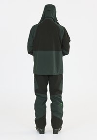 Grüne wasserdichte Jacke mit Kapuze und schwarzen Einsätzen, kombiniert mit passenden Hosen, die über Cargo-Taschen und verstärkte Bereiche verfügen.