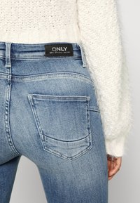 Blå denimjeans med slim fit, med en svart "ONLY"-etikett i midjan och två bakfickor med subtila sömnadsdetaljer.