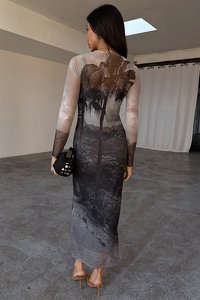 Lang, tettsittende kjole med svart og grå palmeprint, gjennomsiktige lange ermer og gjennomsiktig kant. Kombinert med en svart clutch og hæler.