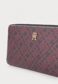 Red and navy wallet featuring a diamond pattern, gold logo detail, textured fabric, and contrasting white stitching along the zipper.