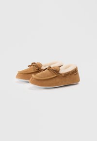 Brown suede moccasin slippers with soft fur lining, rounded toe, decorative bow at the front, and a flat white sole.