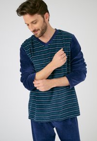 Heren loungewear set met een marineblauwe gestreepte long-sleeve top met een V-hals en effen marineblauwe mouwen, gecombineerd met bijpassende broek. Zachte textuur.