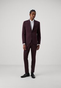 Bordó öltöny, két elülső zsebbel, slim fit kialakítással, textúrált anyagból készült, fehér inggel és fekete fényes cipővel párosítva.