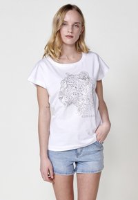 T-shirt en coton blanc à manches courtes, décoré d'un design de silhouette animale en pointillés en strass argentés. Coupe régulière, col rond.