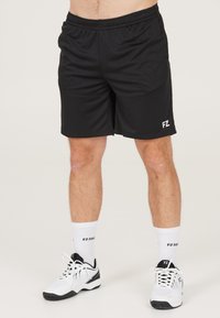 Svarta träningsshorts med elastiskt midjeband och logodetalj i vitt; i kombination med vita strumpor och svart-vita träningsskor.