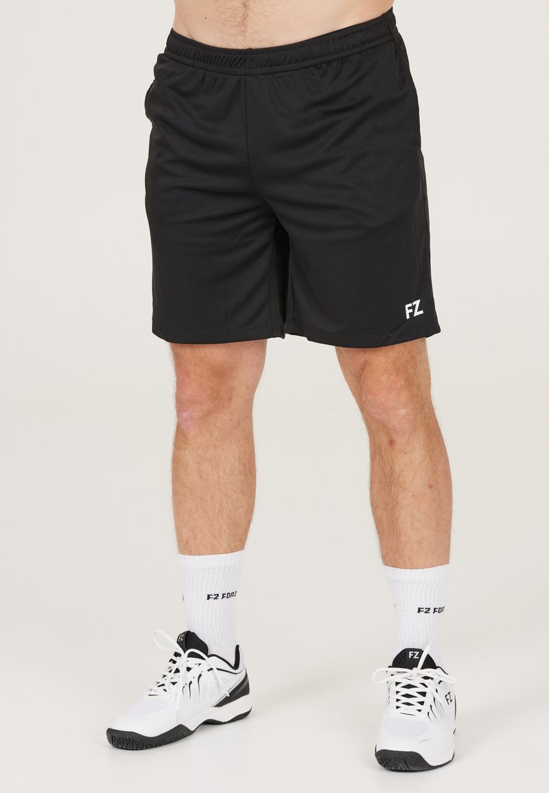 Svarta träningsshorts med elastiskt midjeband och logodetalj i vitt; i kombination med vita strumpor och svart-vita träningsskor.