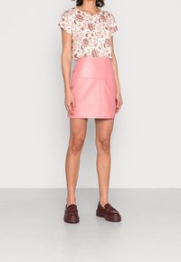 Mini falda de cuero rosa claro con una textura suave, combinada con una blusa blanca con estampado floral. La modelo lleva zapatos de plataforma burdeos.