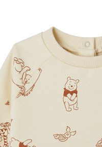 Cremefarbenes Sweatshirt mit einem sich wiederholenden Druck klassischer Cartoonfiguren in Braun, einem gerippten Kragen und Druckknopfverschluss am Hals.