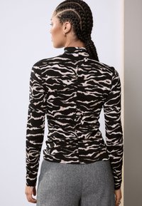 Haut à manches longues noir avec un motif zèbre rose clair. Il présente un col haut et une texture côtelée, associé à un pantalon gris à motif.