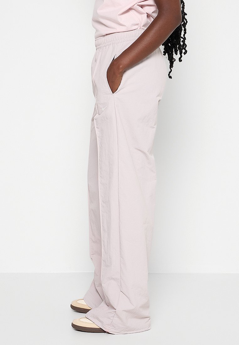 Pantalons larges légers couleur rose clair, avec une taille élastique, des poches latérales et une texture lisse. Présente un branding subtil.
