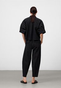 Zwart geruit outfit met een cropped, losse blouse en high-waisted, taps toelopende broeken. De stof heeft een zachte textuur en een subtiel rasterpatroon.