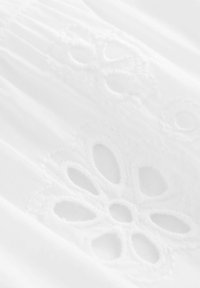 Tela blanca con intrincados bordados florales con centros abiertos y costuras texturizadas, que exhibe un material suave y ligero.