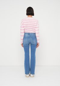 Ριγέ πουλόβερ ροζ και λευκό με μακριά μανίκια, συνδυασμένο με ψηλόμεσα μπλε τζιν. Διαθέτει εφαρμοστή σιλουέτα και διακριτική υφή.