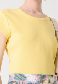 Žlutý vroubkovaný krátký rukáv top s kulatým výstřihem a diskrétním logem, spárovaný s vícebarevným páskem s efektem tie-dye.
