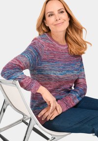 Strickpullover mit einem melierten Muster in rosa und blauen Farbtönen, rundem Halsausschnitt und gerippten Bündchen, kombiniert mit dunklen Jeans.