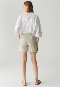 Shorts beige clair avec une coupe ajustée, dotés de deux poches arrière, associés à une chemise blanche ample, avec des détails de couture visibles et des manches courtes.