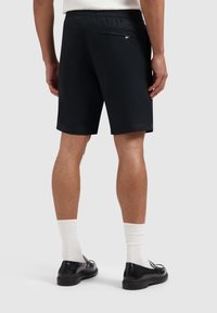 Zwarte shorts met een elastische tailleband en een achterzak. Gladde stof, knielengte ontwerp, gecombineerd met witte sokken en zwarte schoenen.