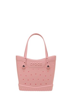 Różowa torba typu tote Crocs z okrągłymi perforacjami, dwoma paskami na ramię i teksturowanym, przypominającym podeszwę, dolnym brzegiem.